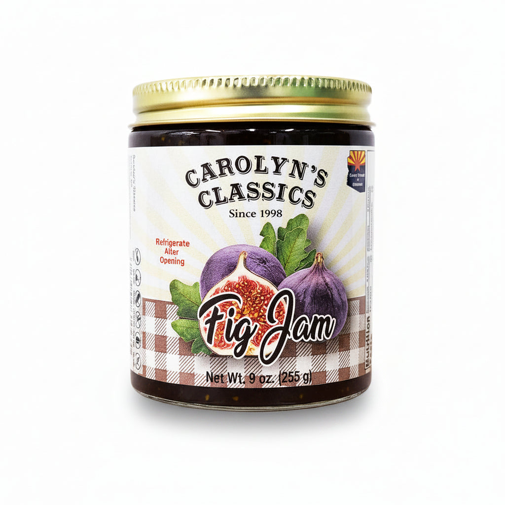 A jar of Carolyn's Classics Fig Jam sits on a wooden tabletop against a plain light gray wall. The gold-lidded jar has a white label with purple fig illustrations and the brand name Carolyn's Classics.