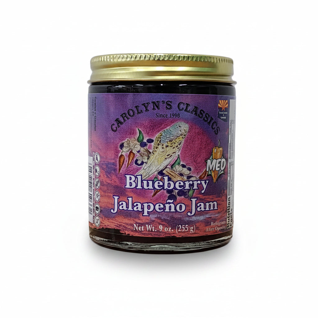 A small glass jar of Candy's Classic Blueberry Jalapeño Jam sits on a wooden tabletop against a plain light gray wall.